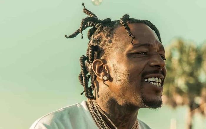 Sauce Walka with plaited hair and showing his teeth