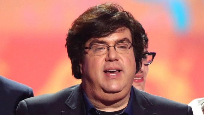 Dan Schneider on glasses wearing a black suit on stage