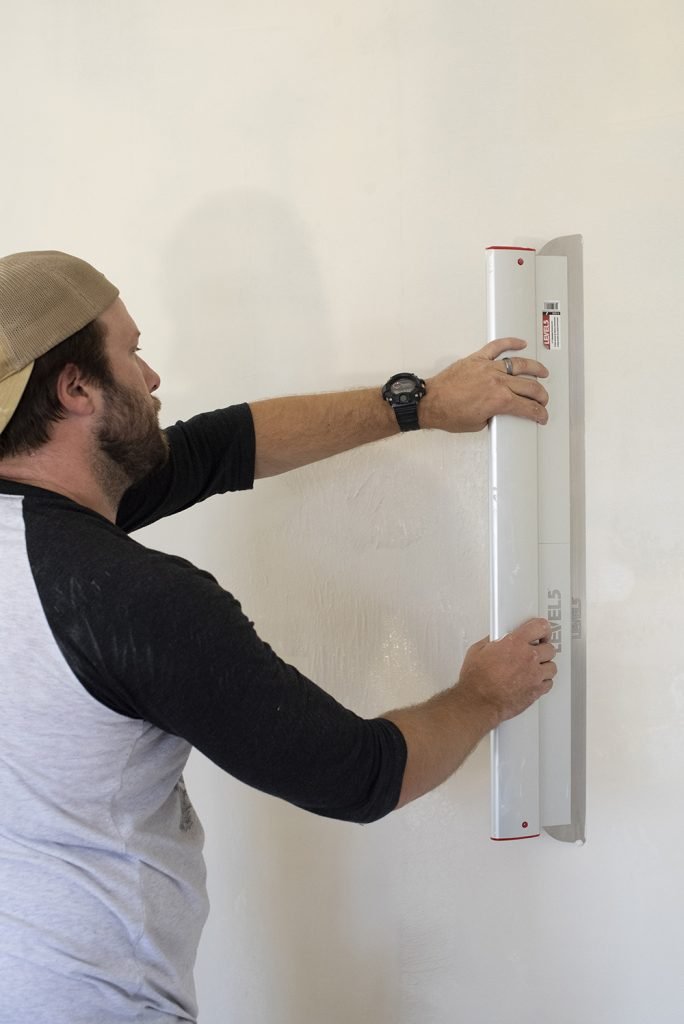 man using leveling tool to skim coat the wall