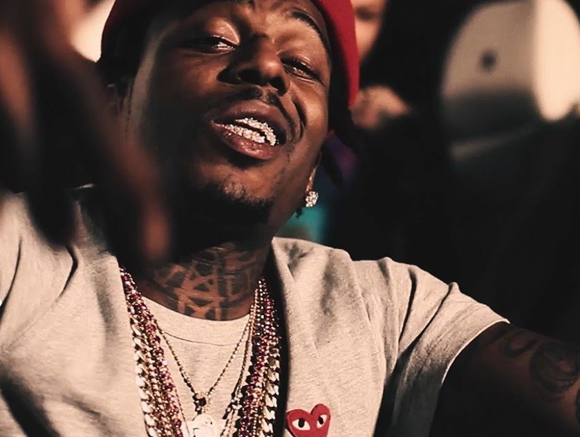 Sauce Walka sitting on the ground while wearing a red face cap